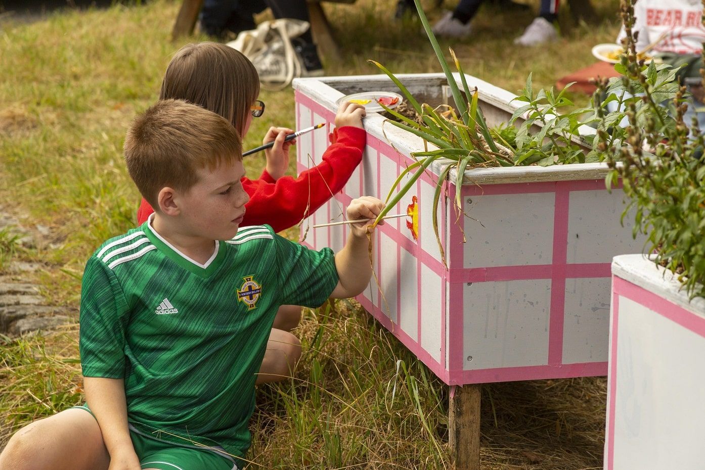 Two young children paint individual squares on a wooden planter in GRIT Studios' community garden.